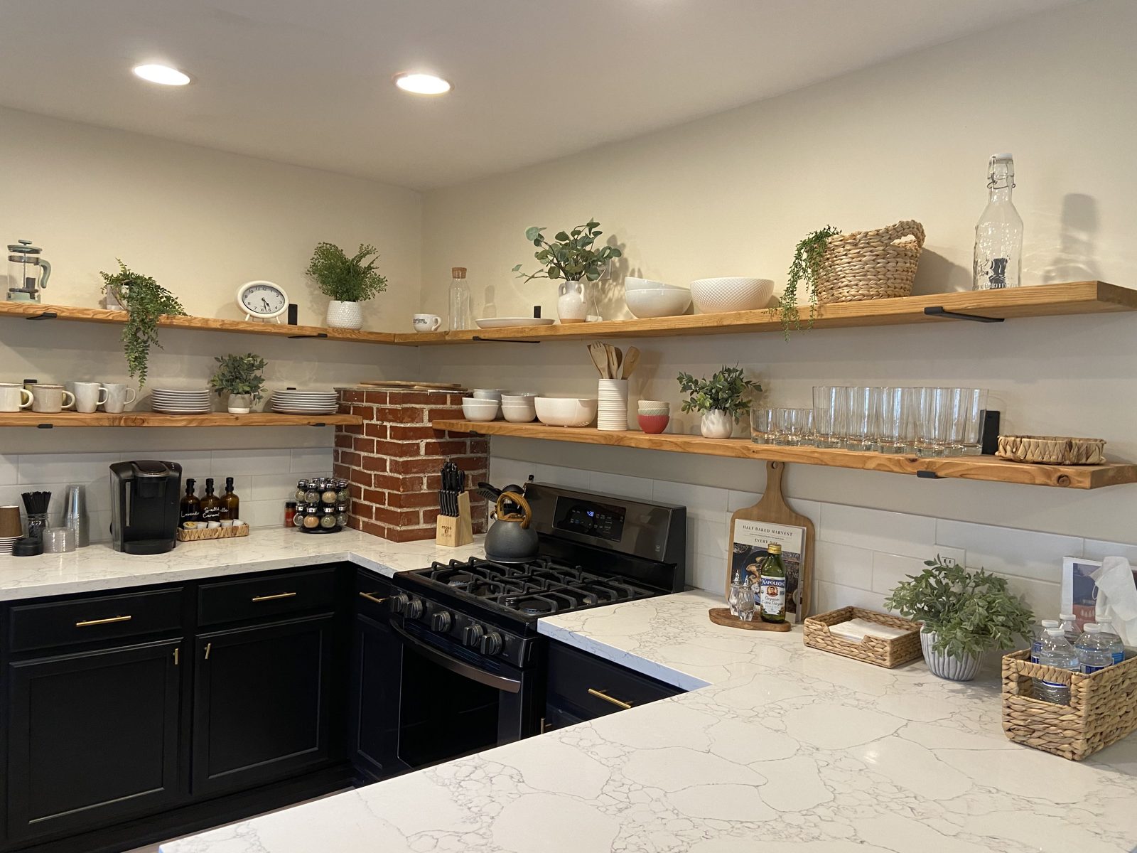 Finished kitchen with black cabinets, quartz counters, exposed brick and open shelving
